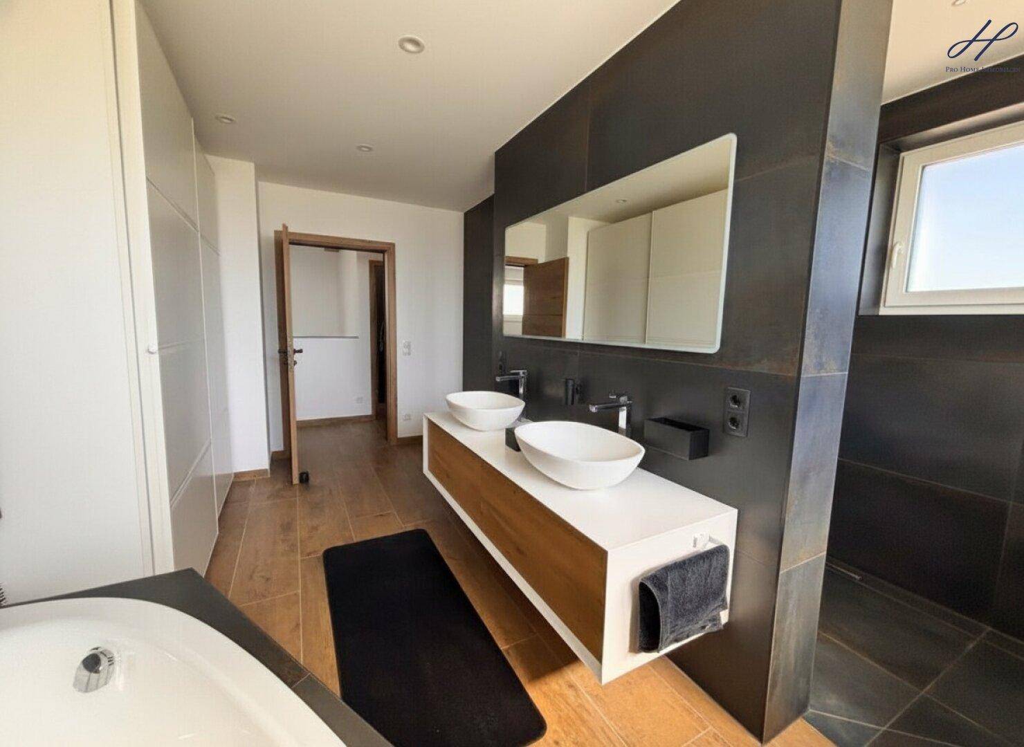 Stilvolles Badezimmer mit Doppelwaschbecken, Badewanne und dunklen Wandfliesen, die einen Kontrast bilden.