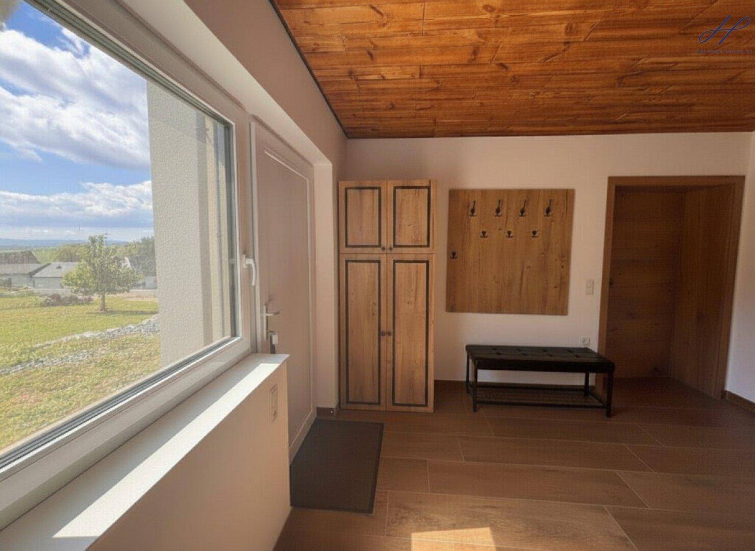 Heller Eingangsbereich mit Holzdecke, Garderobe und großem Fenster mit Blick ins Grüne.