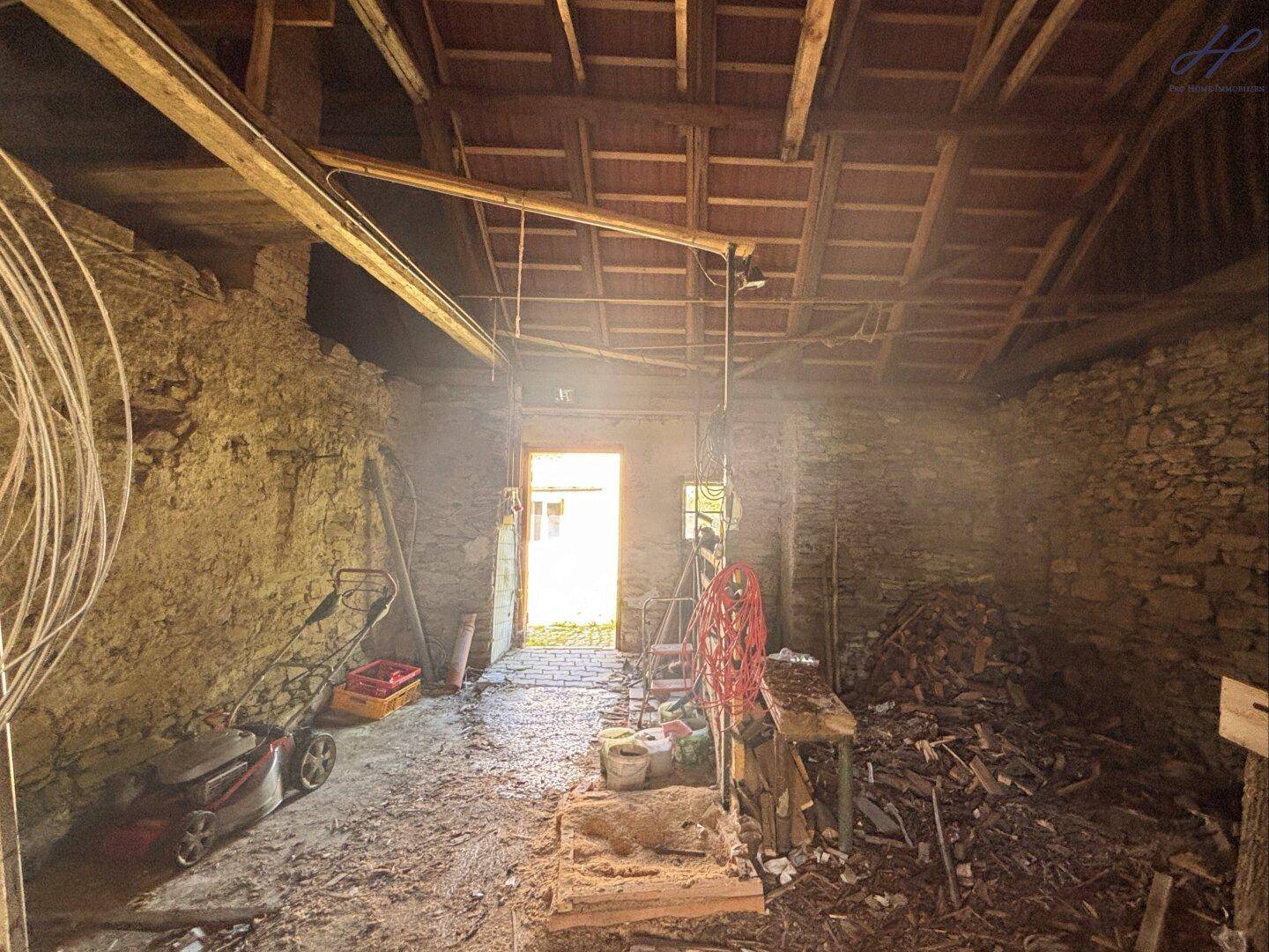 Rustikaler Innenraum eines Nebengebäudes mit Holzbalken, Steinwänden und Geräten.