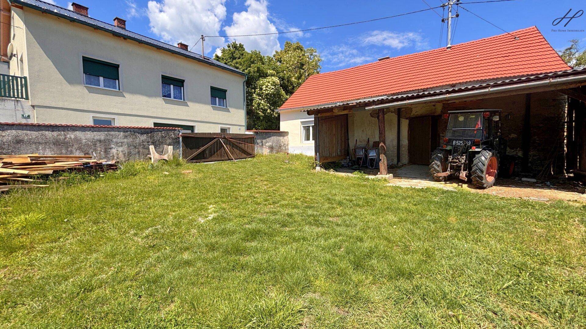 Weitläufiger Gartenbereich hinter dem Haus mit Blick auf ein Nachbargebäude und Holzstapel.
