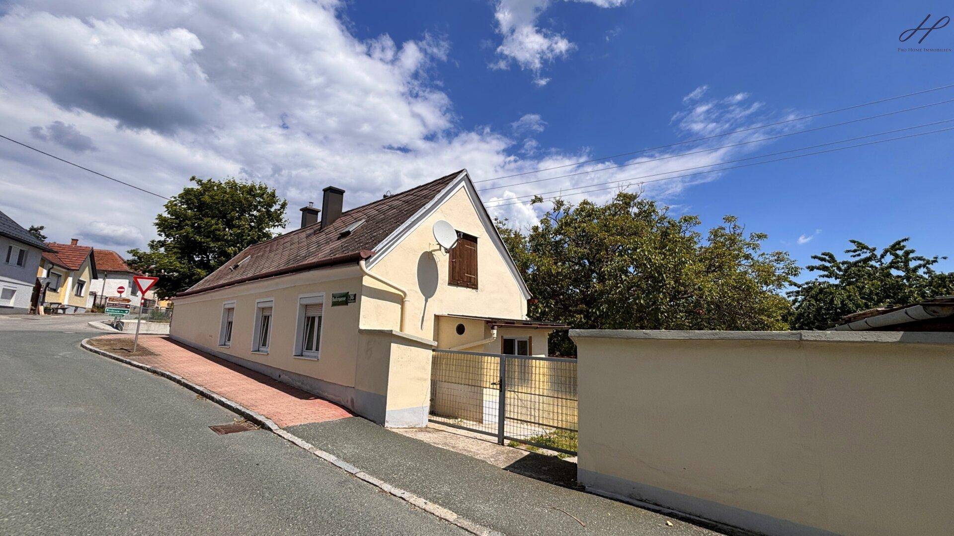 Ländliches Haus an einer Straße mit schrägem Dach und traditioneller Fassade unter blauem Himmel.