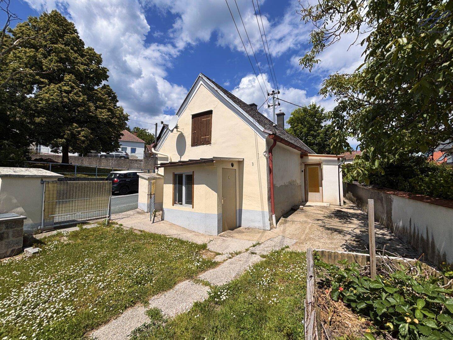 Seitenansicht des Hauses mit Gartenbereich, gepflastertem Weg und Blick auf die Umgebung.