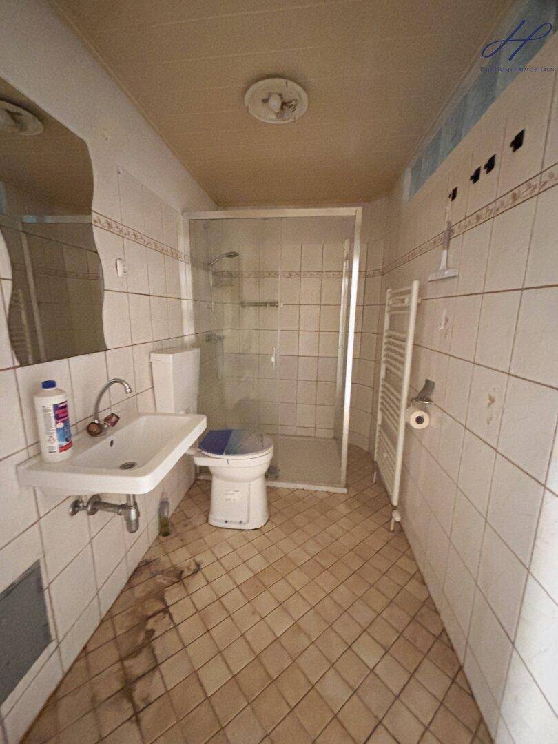 Einfaches Badezimmer mit Dusche, WC, Waschbecken und Fliesen im 80er-Jahre-Stil.