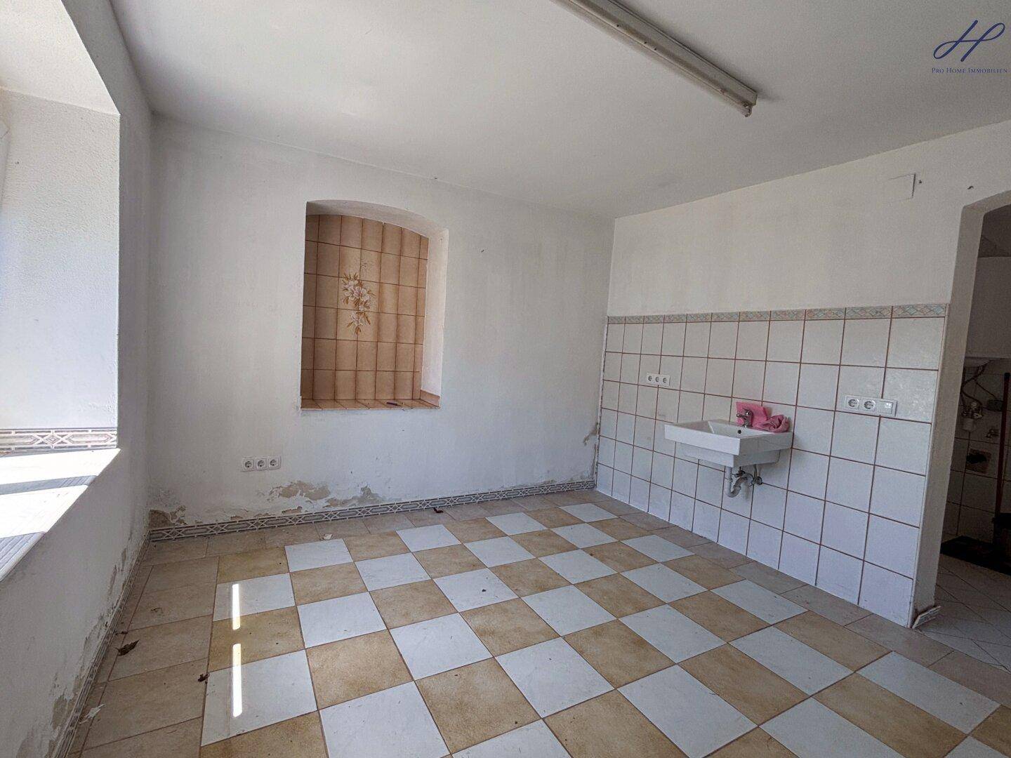 Geräumiger Raum mit kariertem Fliesenboden, Waschbecken und einem Fenster.