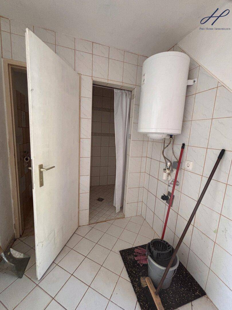 Kleiner Raum mit Warmwasserboiler, Fliesen und Zugang zu einer Duschkabine.