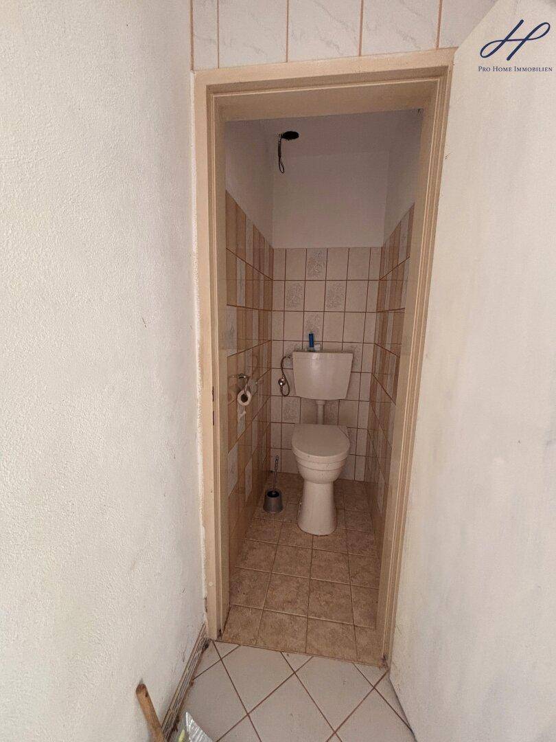 Separate Toilette mit Fliesen an Wänden und Boden, in einfachem Zustand.