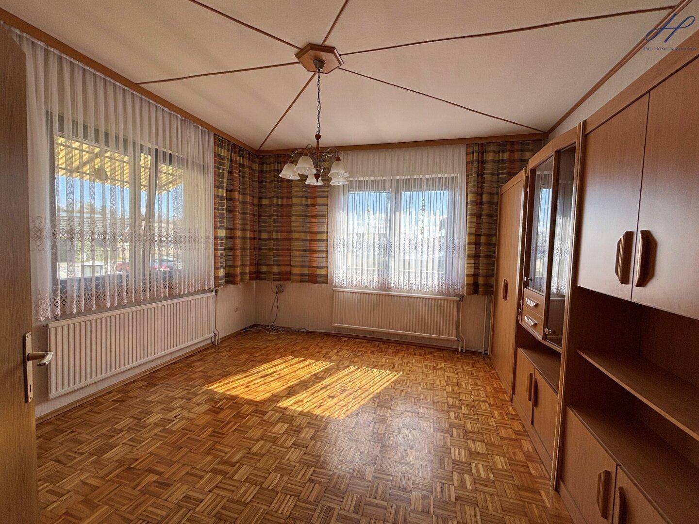 Helles Wohnzimmer mit Parkettboden, gemusterter Decke und großen Fenstern mit viel Sonnenlicht.