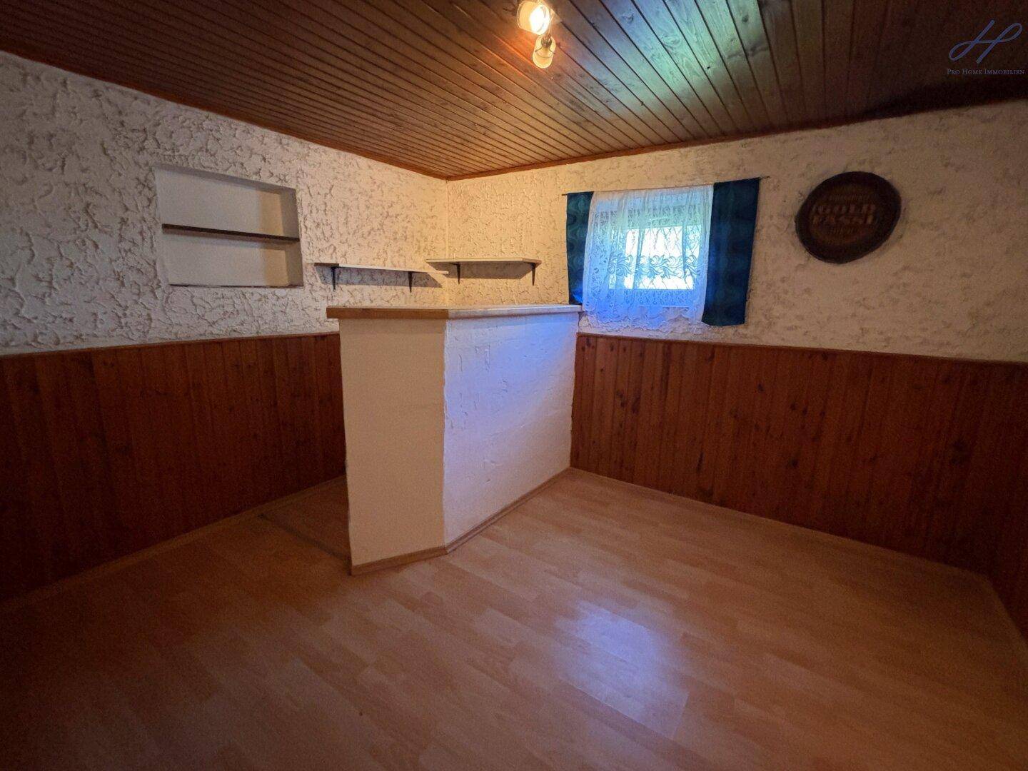 Raum mit Holzvertäfelung, Laminatboden und einer kleinen Theke, ideal als Hobbyraum.