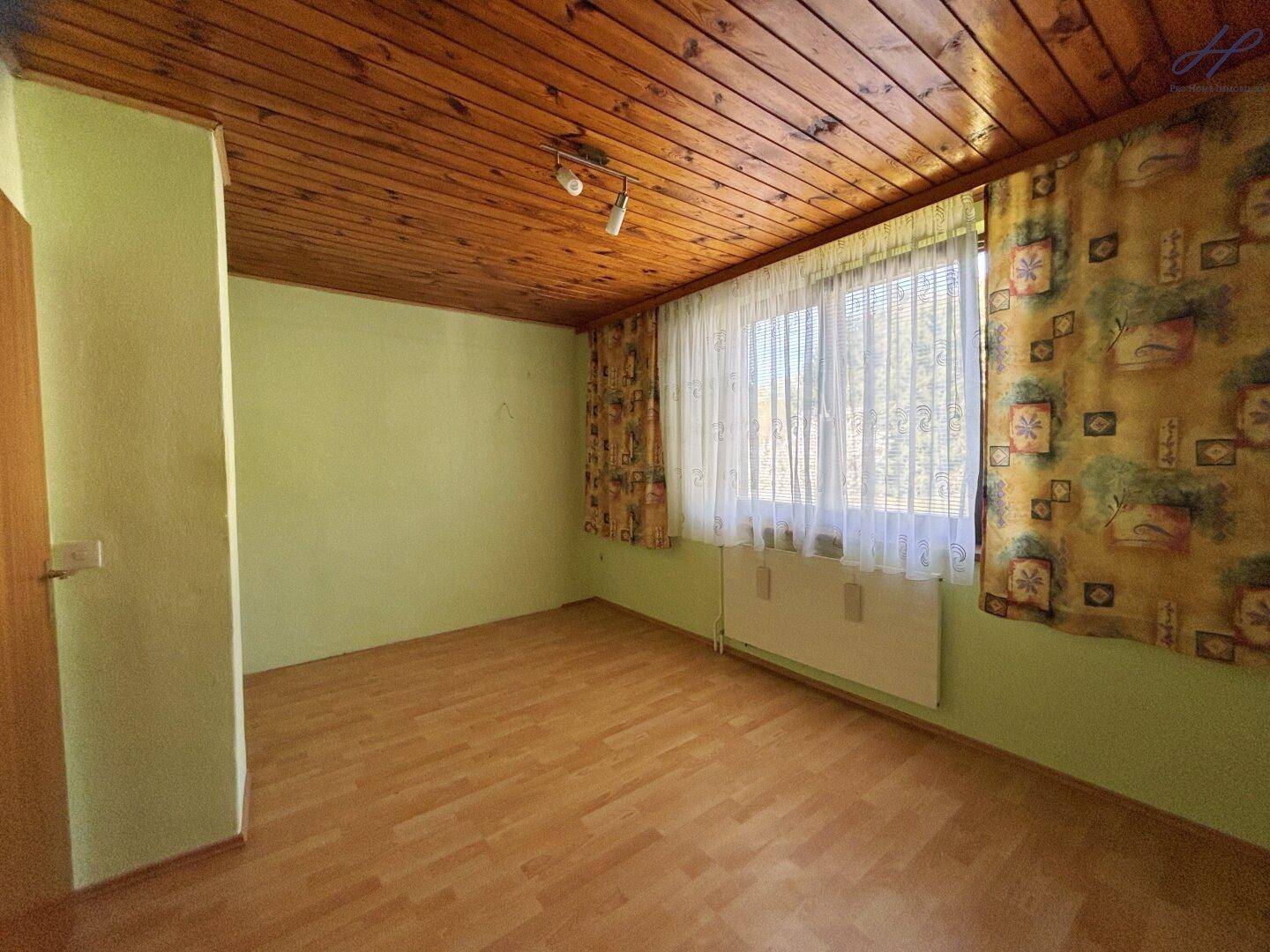 Schlafzimmer mit grünen Wänden, Holzdecke und Laminatboden, hell durch großes Fenster.