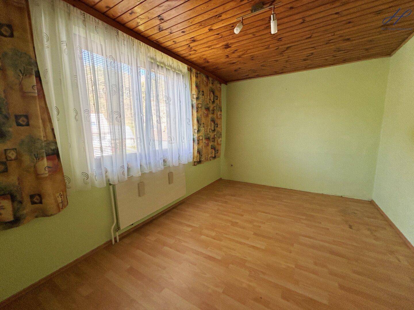 Schlafzimmer mit grünen Wänden, Holzdecke und Laminatboden, hell durch großes Fenster.