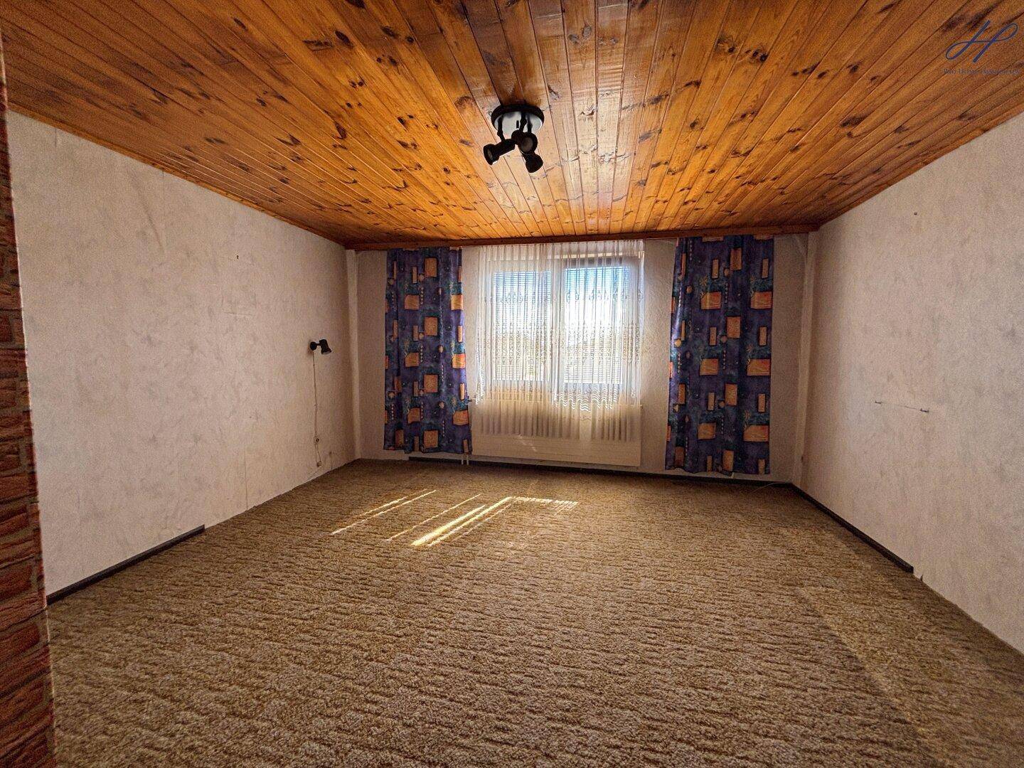 Wohnzimmer mit Teppichboden, Holzdecke und Fenster, das viel Tageslicht hereinlässt.
