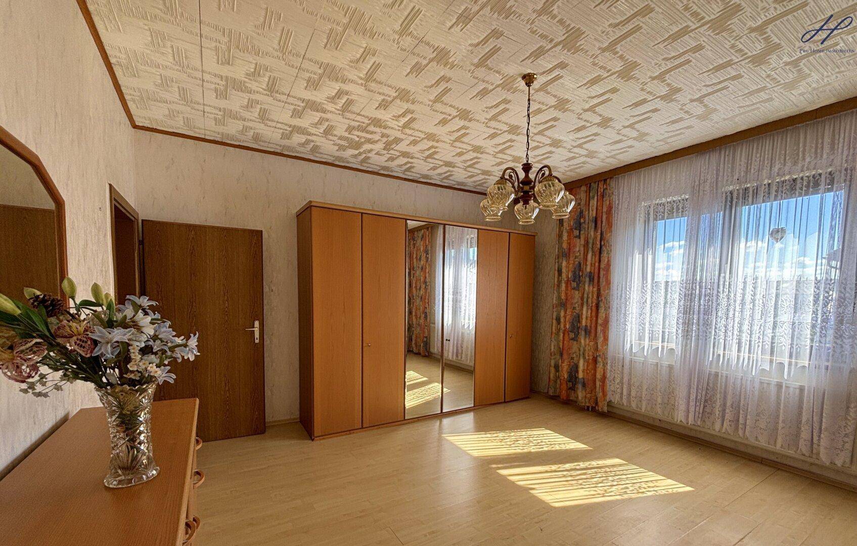 Schlafzimmer mit hellem Laminatboden, Spiegelschrank und Fenster mit Blick nach draußen.