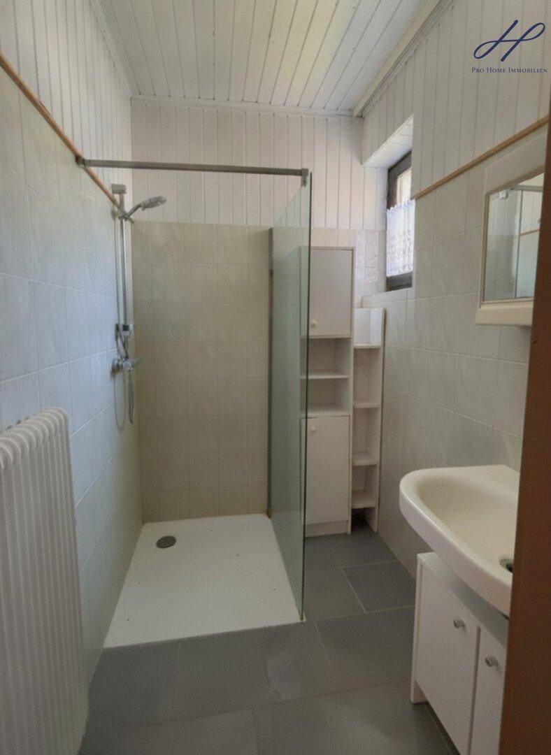 Badezimmer mit Duschkabine, Waschbecken und Fenster, einfach gefliest und funktional.