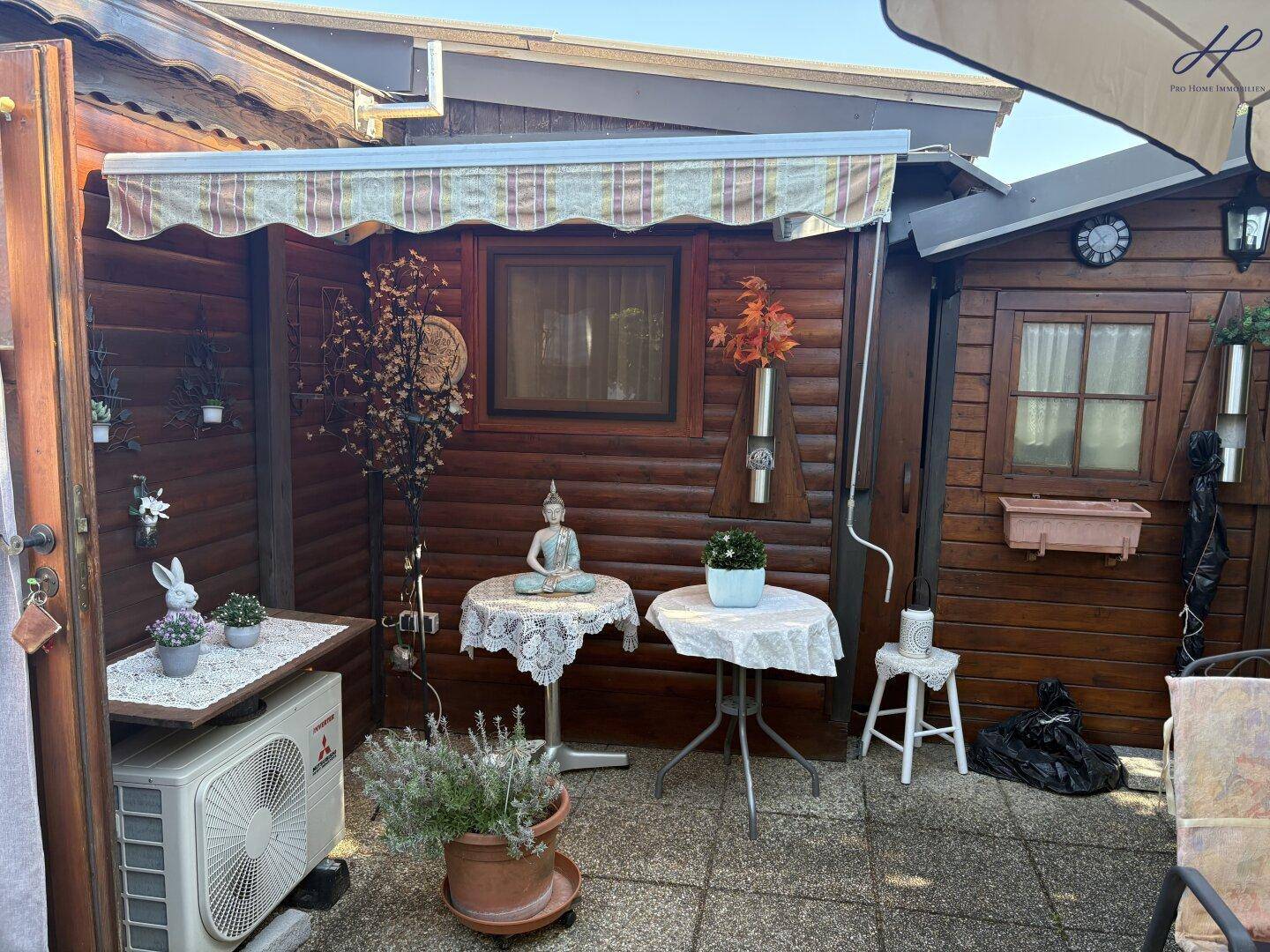 Detailansicht der Terrasse mit Holzhütte, Markise und dekorativen Elementen, ideal für sonnige Tage.