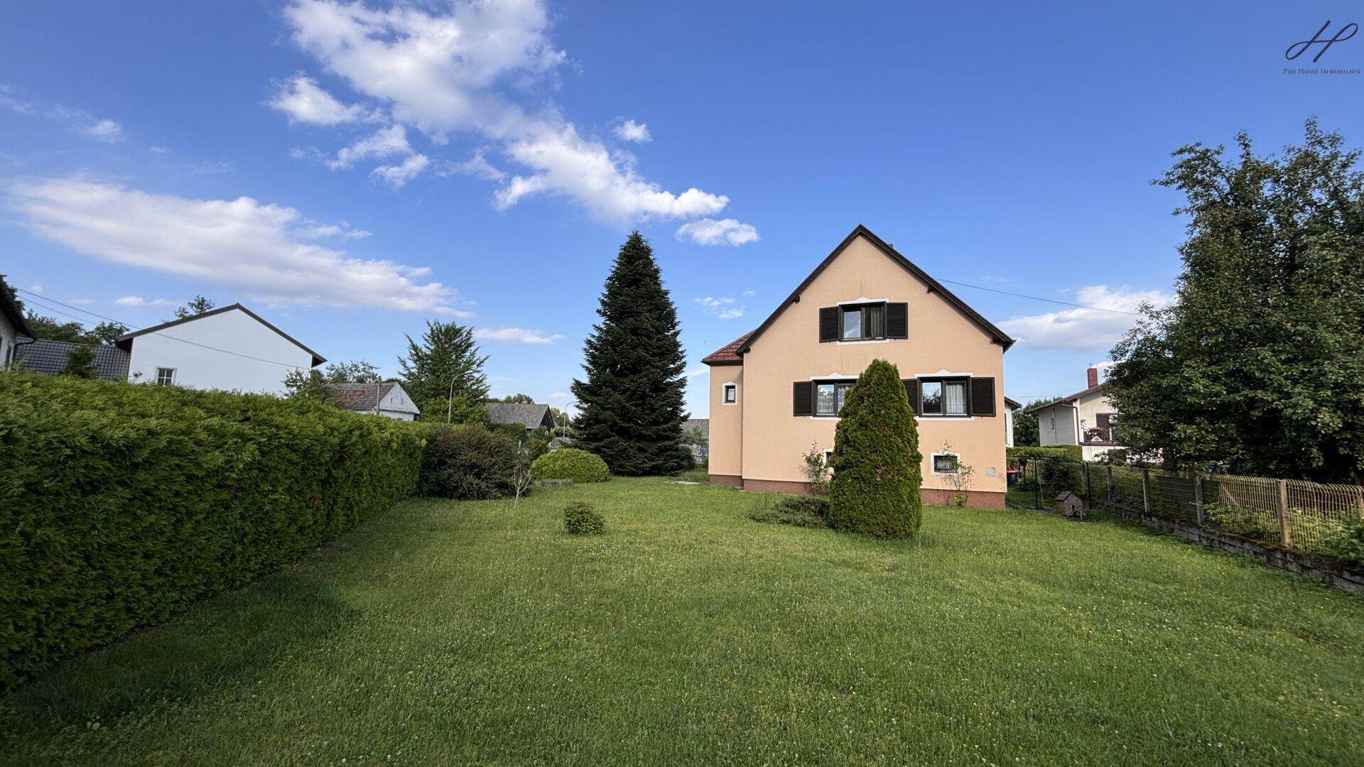 Weitläufiger Gartenbereich neben dem Haus mit hohen Bäumen, Hecken und Rasenfläche.