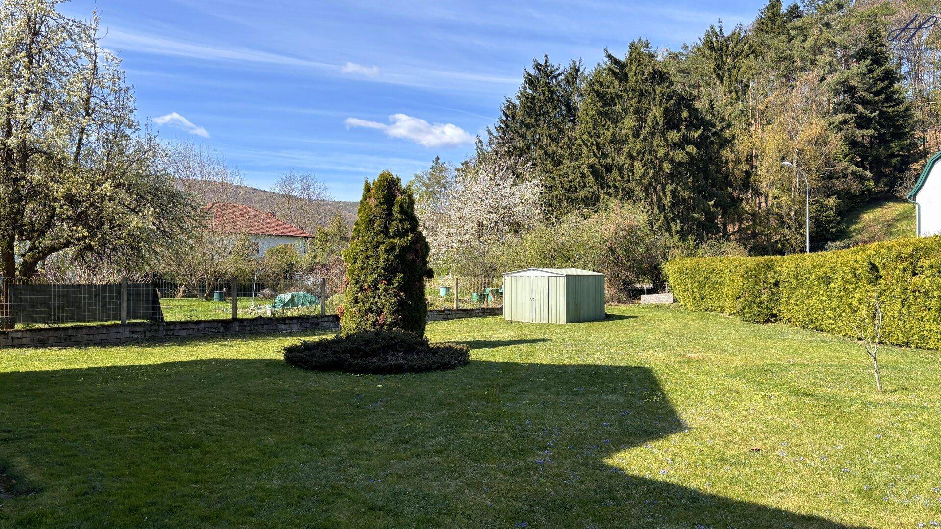 Großer, gepflegter Garten mit Rasenfläche, Gartenhaus und Blick auf die bewaldeten Hügel.