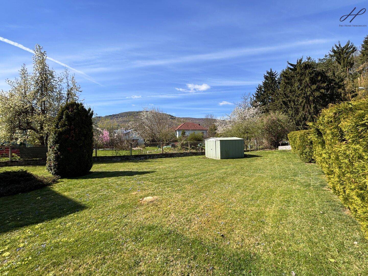 Weitläufiger Garten mit Rasen, Gartenhaus und Panoramablick auf die umliegende Natur.