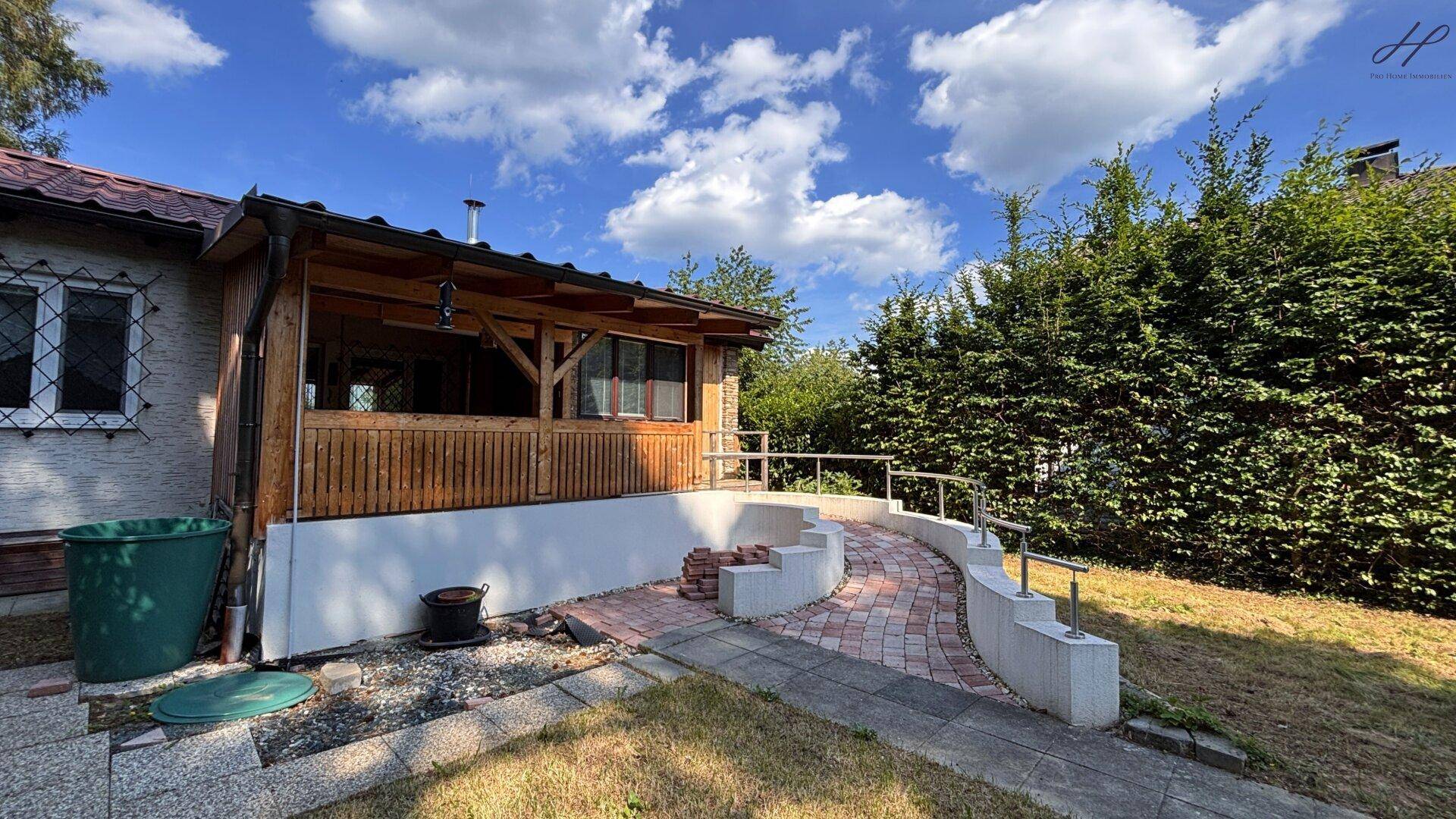 Seitenansicht des Hauses mit der überdachten Veranda und einem geschwungenen Weg dorthin.