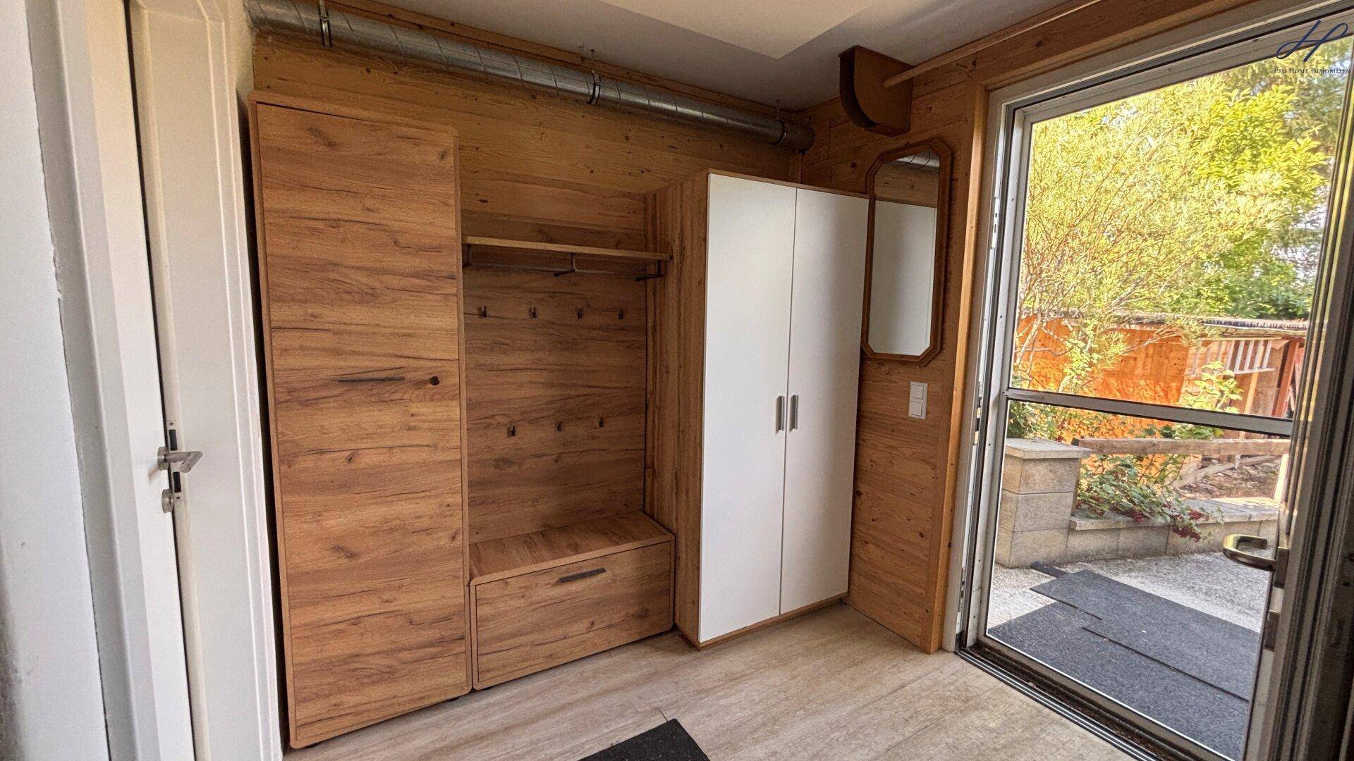 Heller Flur mit Holzvertäfelung, Einbauschrank und einer Glastür zum Außenbereich.