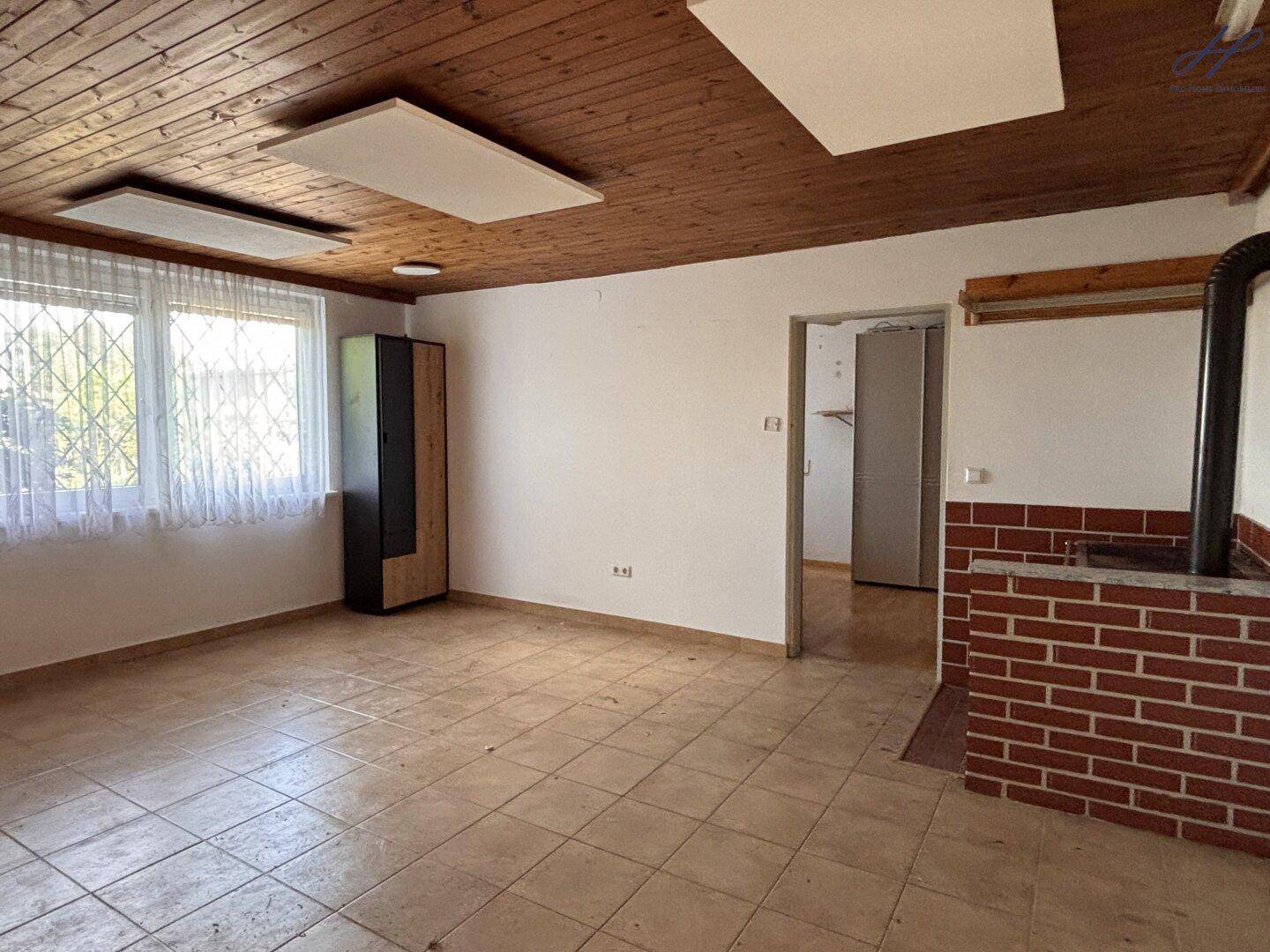 Wohnzimmer aus einer anderen Perspektive mit Fliesenboden, Holzdecke und einem Kleiderschrank.