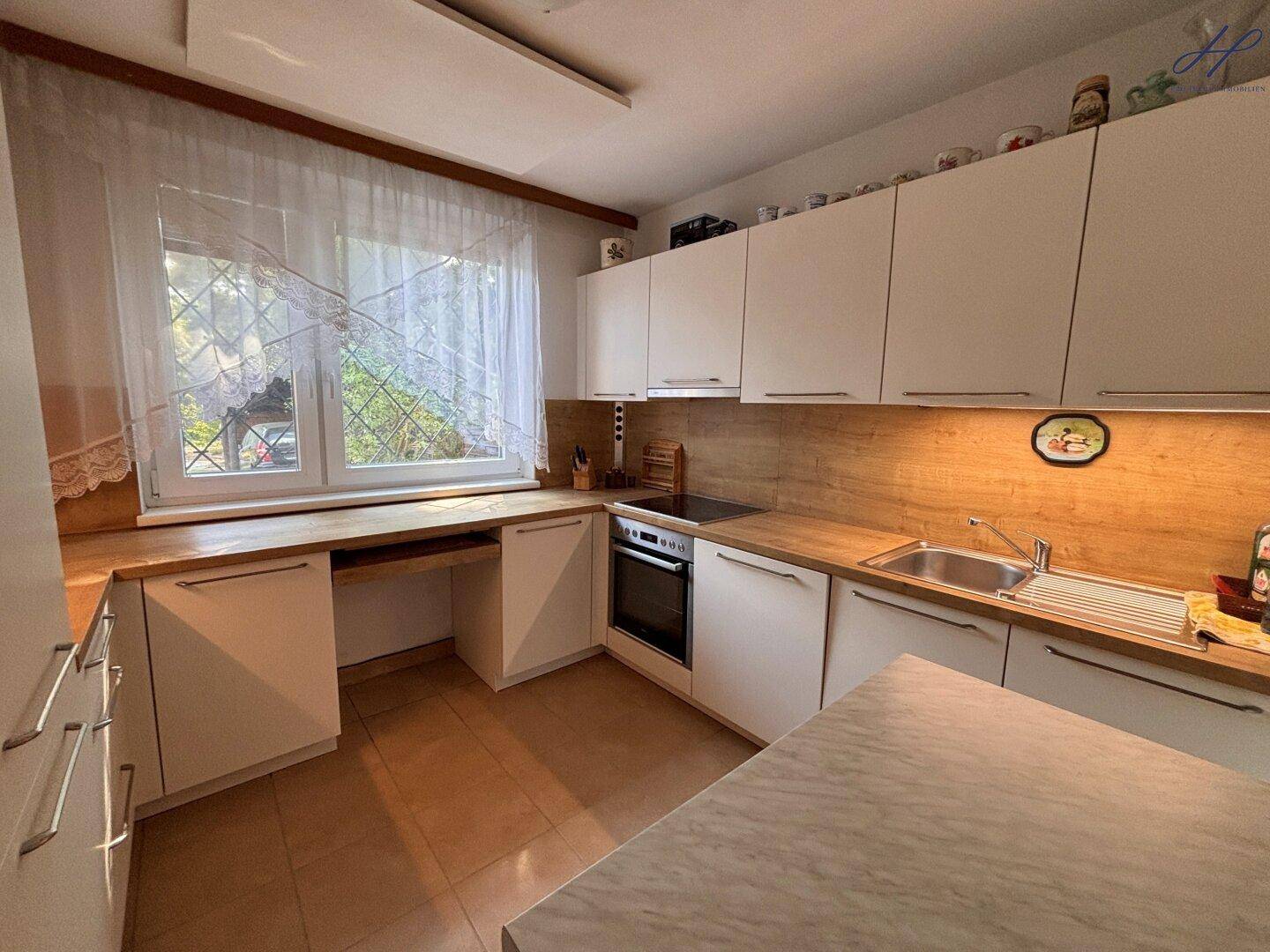 Küche mit weißen Schränken, Holz-Arbeitsplatten, Spüle und einem Fenster mit Blick in den Garten.