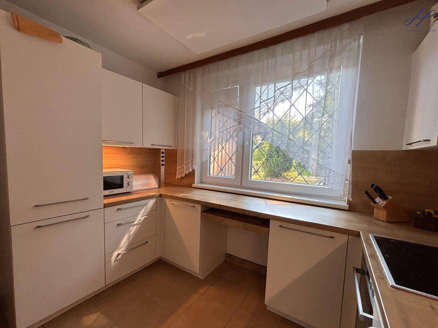 Küche aus einer anderen Perspektive mit weiteren weißen Schränken, Holz-Arbeitsplatten und einer Mikrowelle.