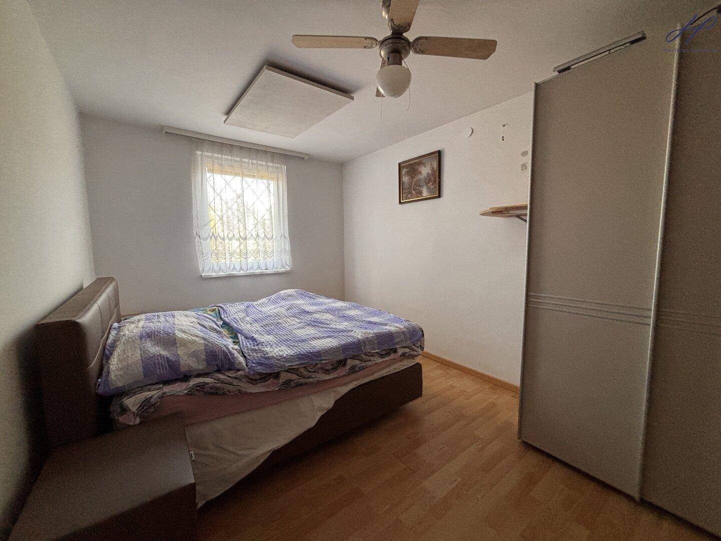 Schlafzimmer mit Bett, Kleiderschrank, Holzfußboden und einem Deckenventilator.