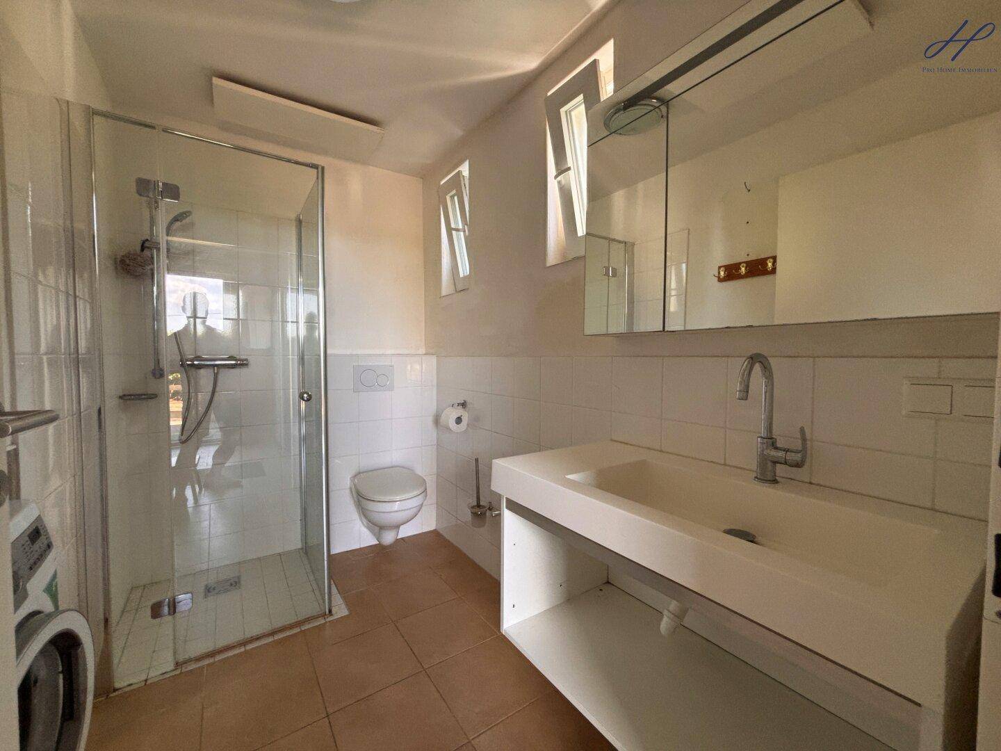 Badezimmer mit Duschkabine, Toilette, Einzelwaschbecken und einer Waschmaschine.