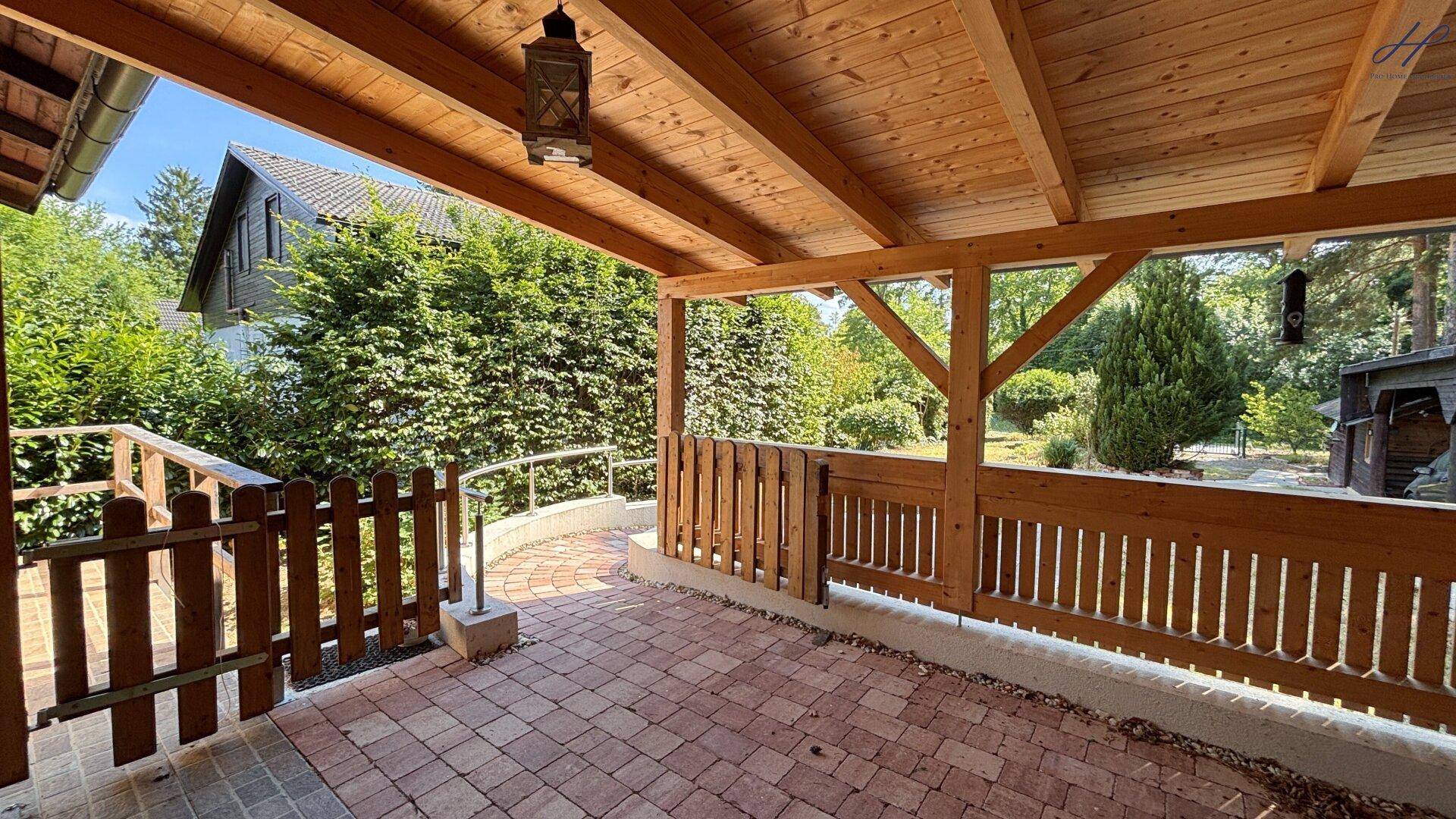 Überdachte Terrasse aus einer anderen Perspektive mit Holzgeländer und umgebendem Grün.