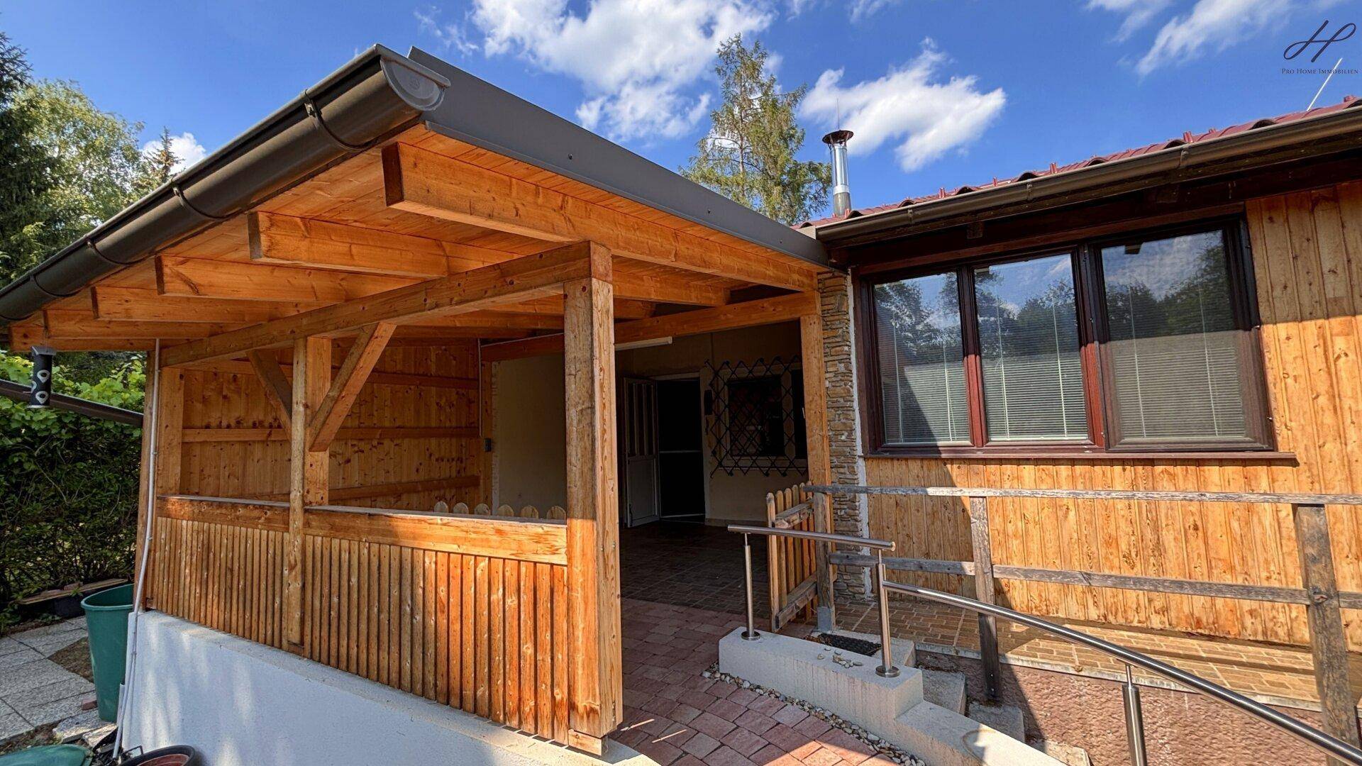 Überdachter Veranda-Eingang zum Haus, mit Holzkonstruktion und gepflastertem Bereich.
