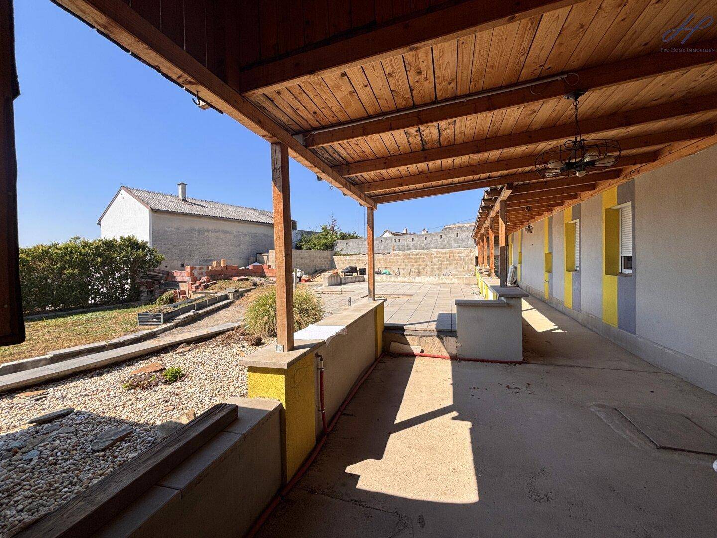 Überdachter Außenbereich mit Holzbalken und Blick auf den Gartenbereich im Umbau.