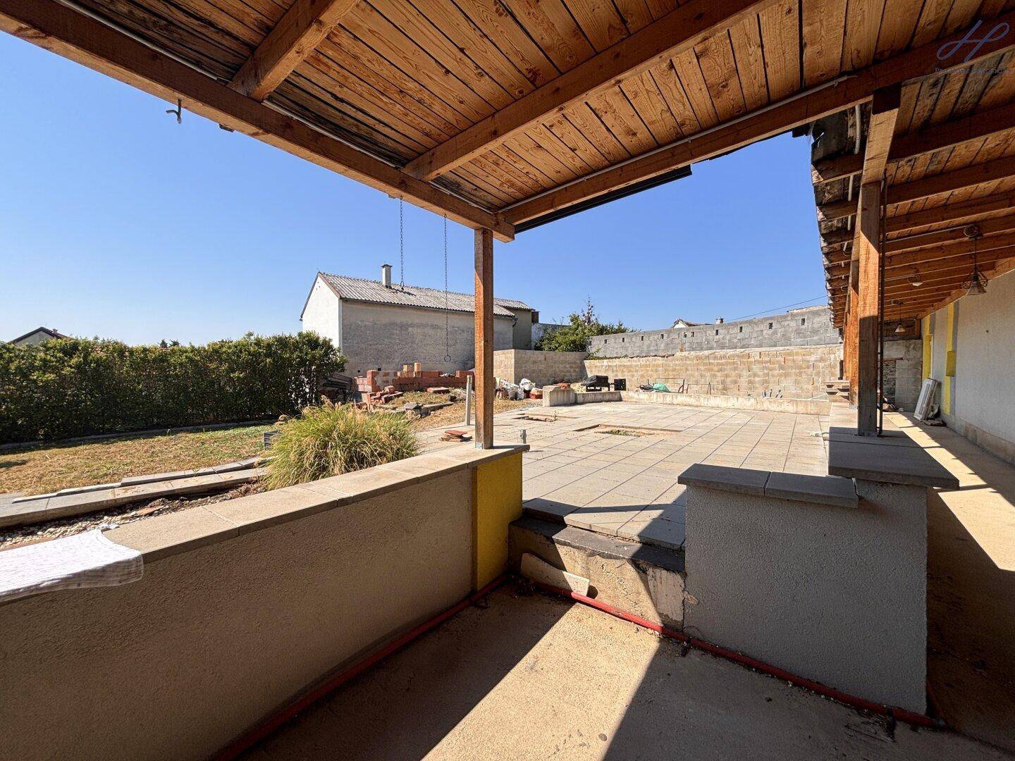 Überdachter Terrassenbereich mit Holzdach und Blick auf den Gartenbereich unter freiem Himmel.