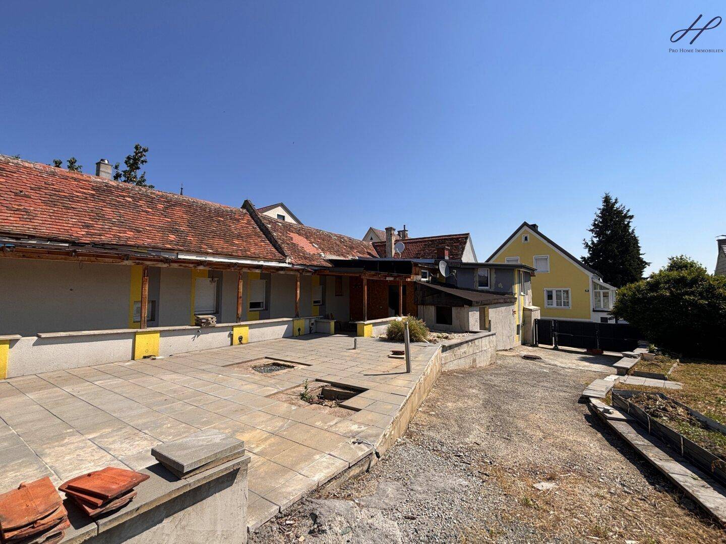 Gesamtansicht des Gebäudes mit gepflastertem Vorplatz und angrenzendem Gartenbereich.