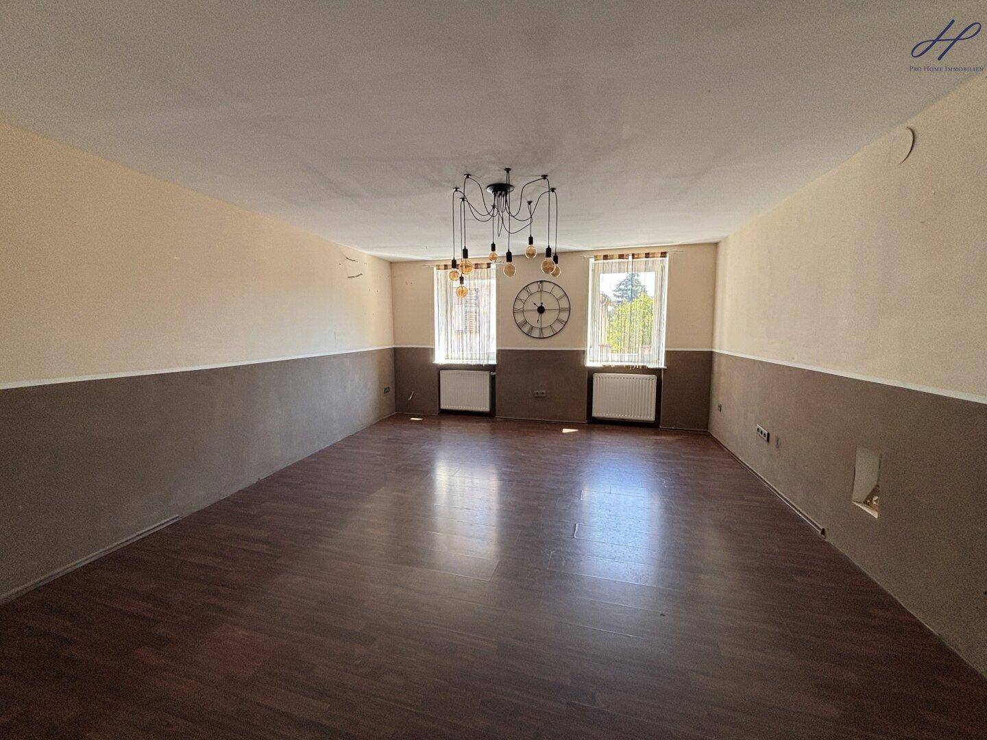 Großer Raum mit Laminatboden, zweifarbigen Wänden und modernen Hängelampen.