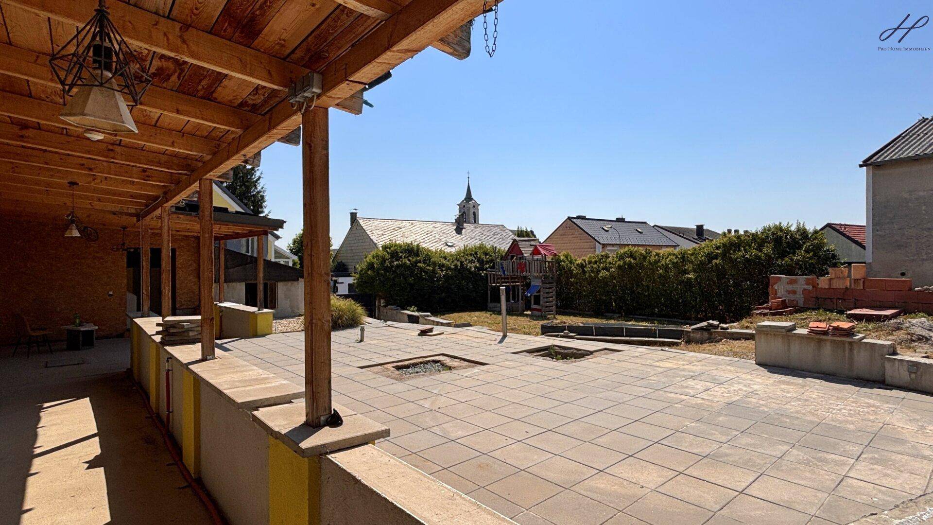 Überdachte Terrasse mit Blick auf einen Spielplatz und die umliegende Nachbarschaft mit Kirche.