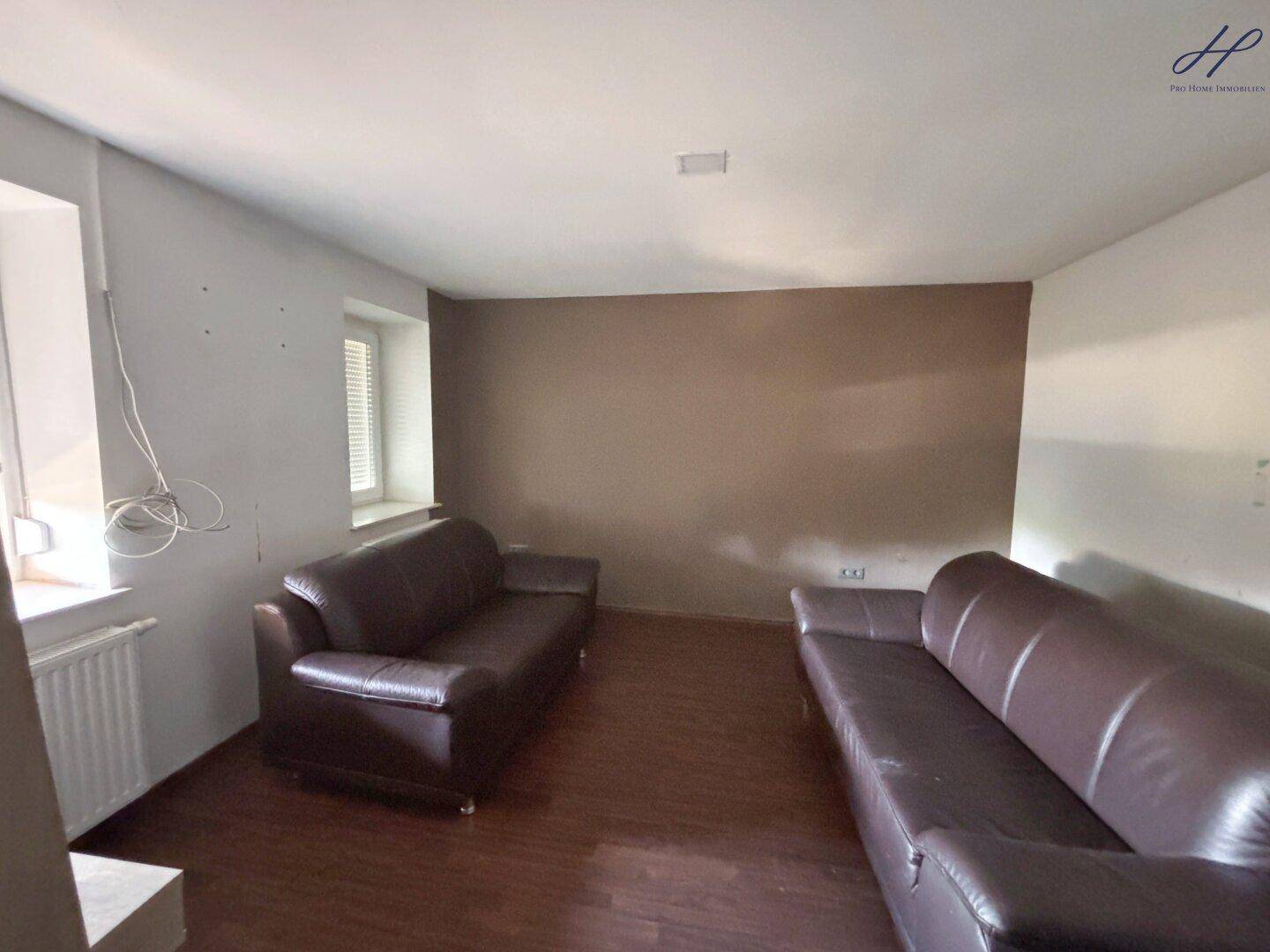 Geräumiges Wohnzimmer mit dunklem Laminatboden und zwei braunen Ledersofas.