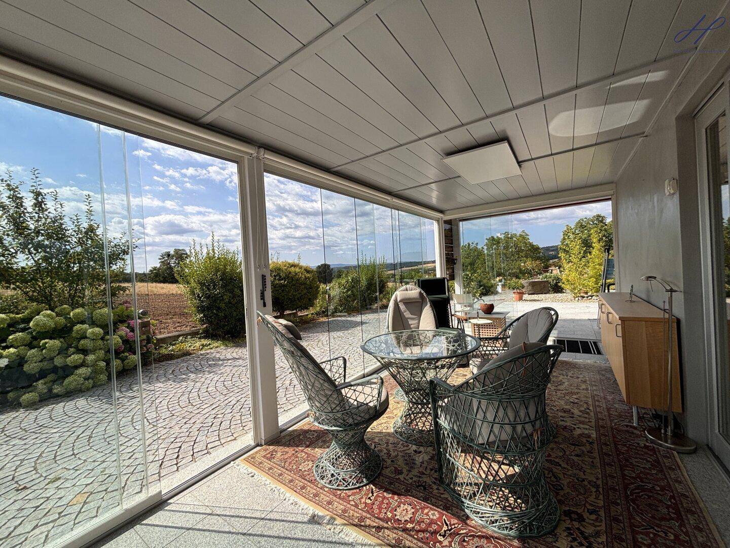 Heller Wintergarten mit Rattanmöbeln und Panoramablick auf die umliegende Natur.