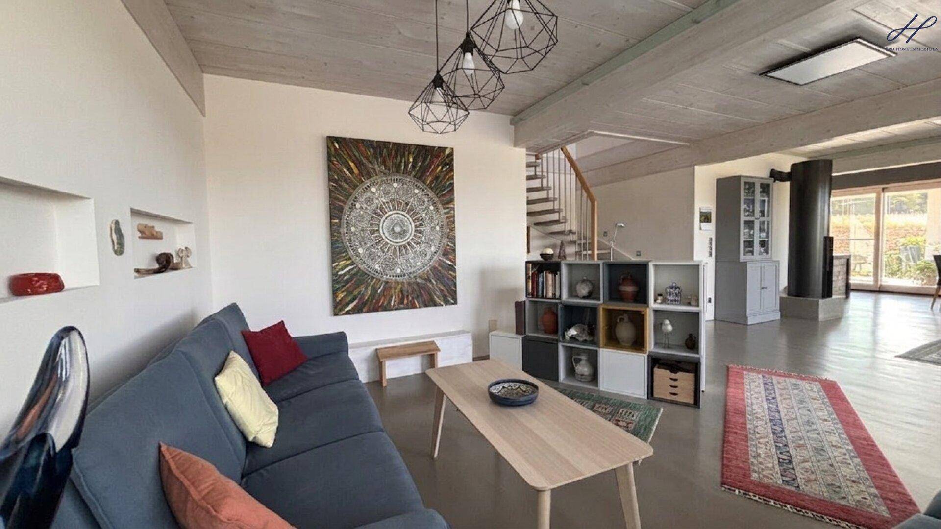 Gemütlicher Wohnbereich mit Sofa, Kunstwerken und einer eleganten Holztreppe im Hintergrund.
