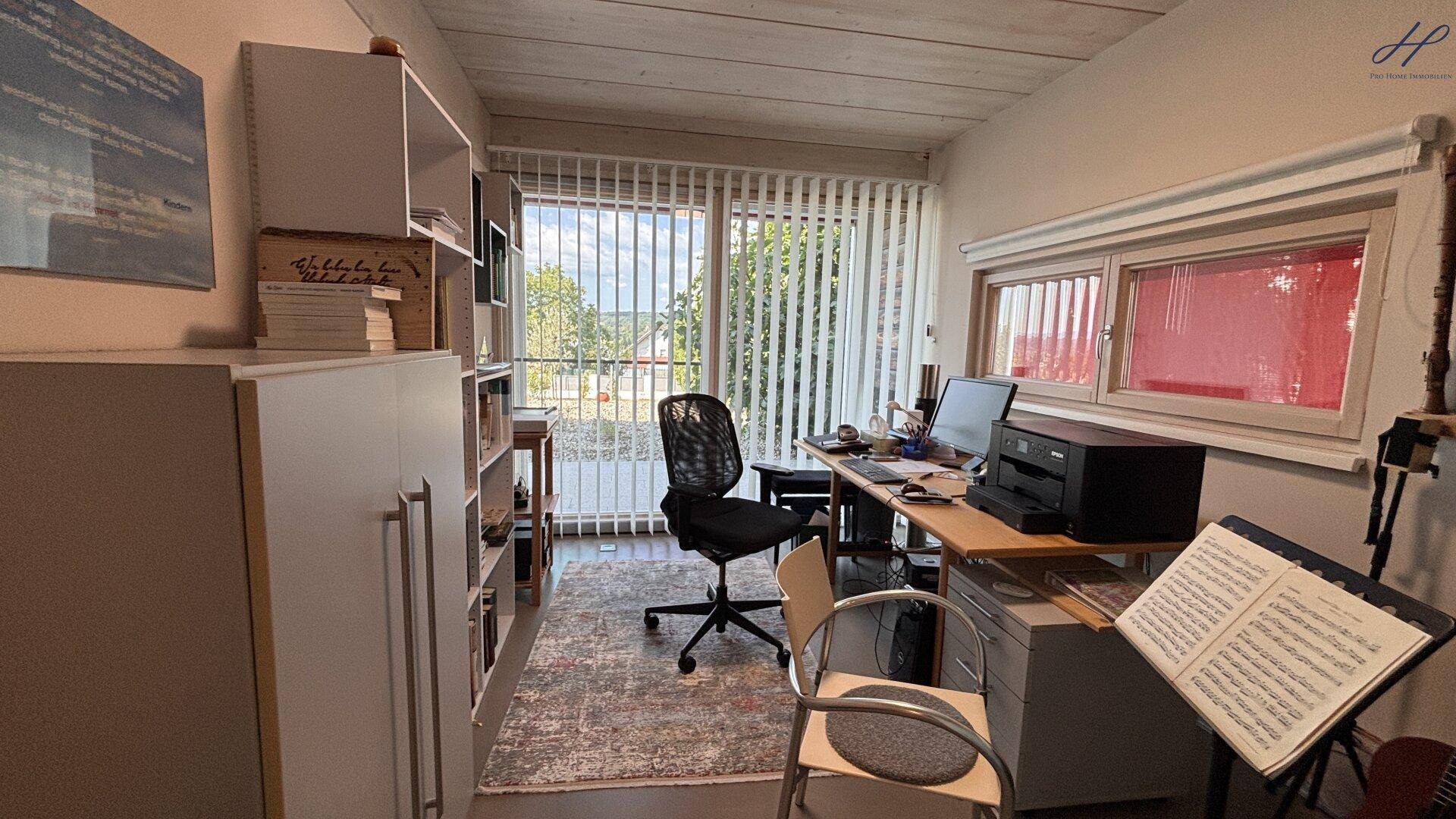 Helles Arbeitszimmer mit Schreibtisch, Bücherregalen und Blick ins Grüne.