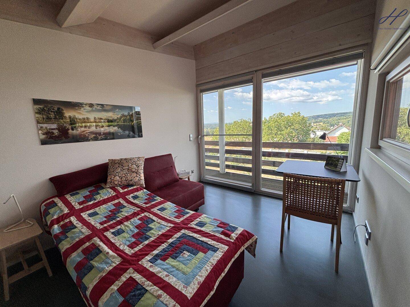 Komfortables Schlafzimmer mit Bett, Schreibtisch und weitem Blick in die Natur.