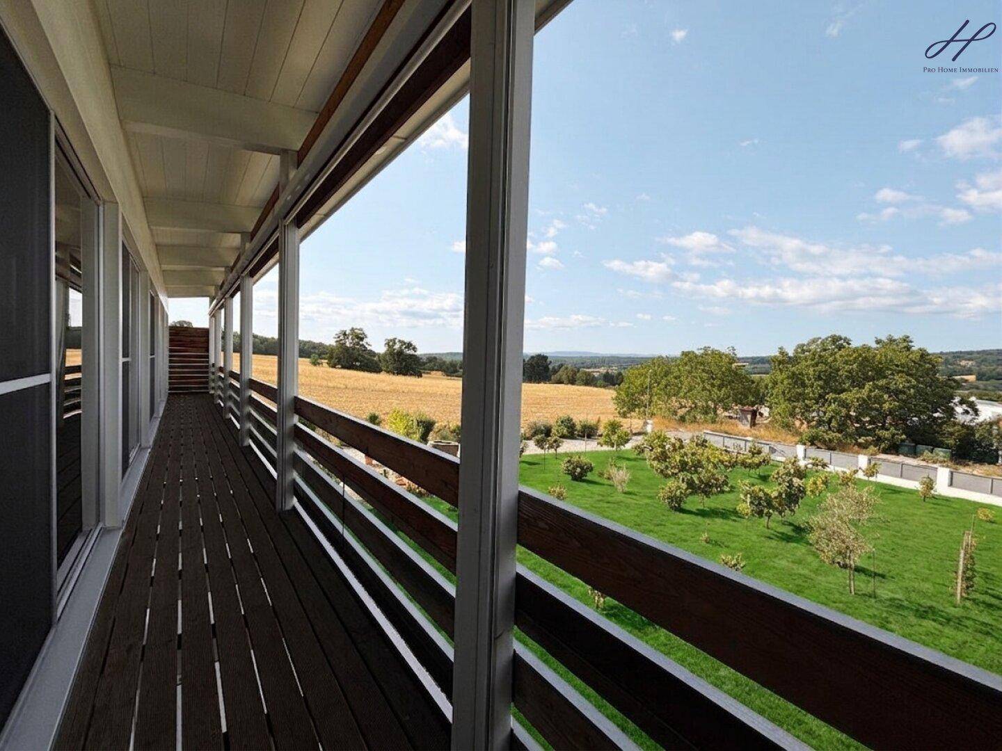 Langer Holzbalkon mit weitem Blick über die Felder und den Garten des Anwesens.