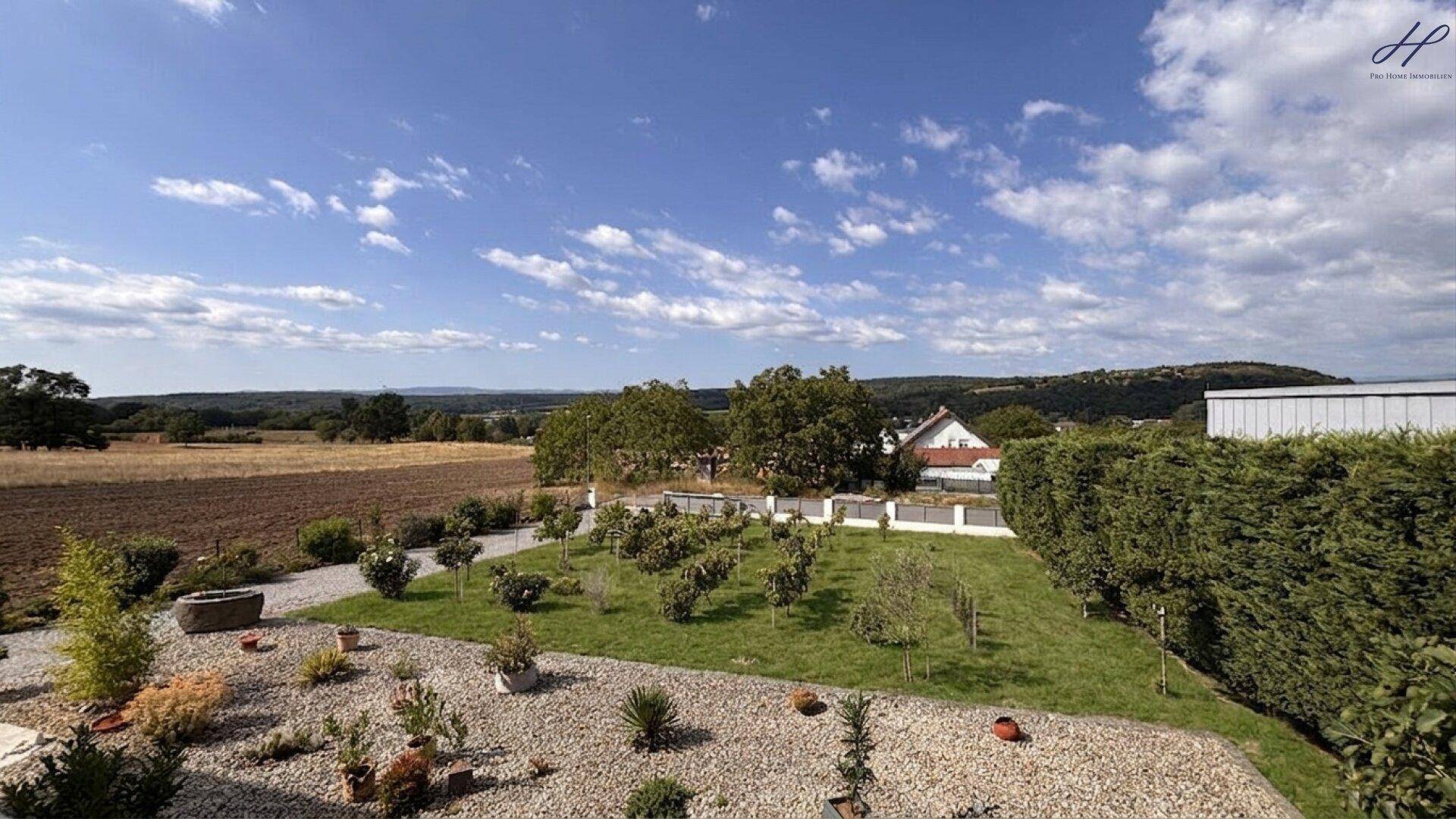 Gepflegter Gartenbereich mit Rasen, Ziersträuchern und weitem Blick in die Landschaft.