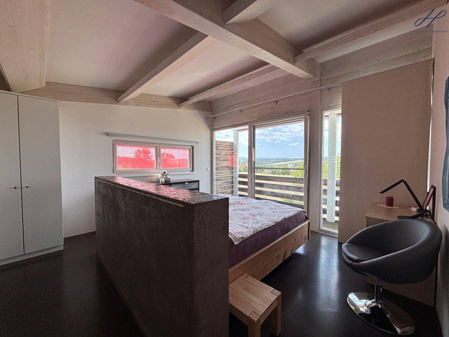 Schlafzimmer mit Holzbett, großen Fenstern und Zugang zum Balkon.