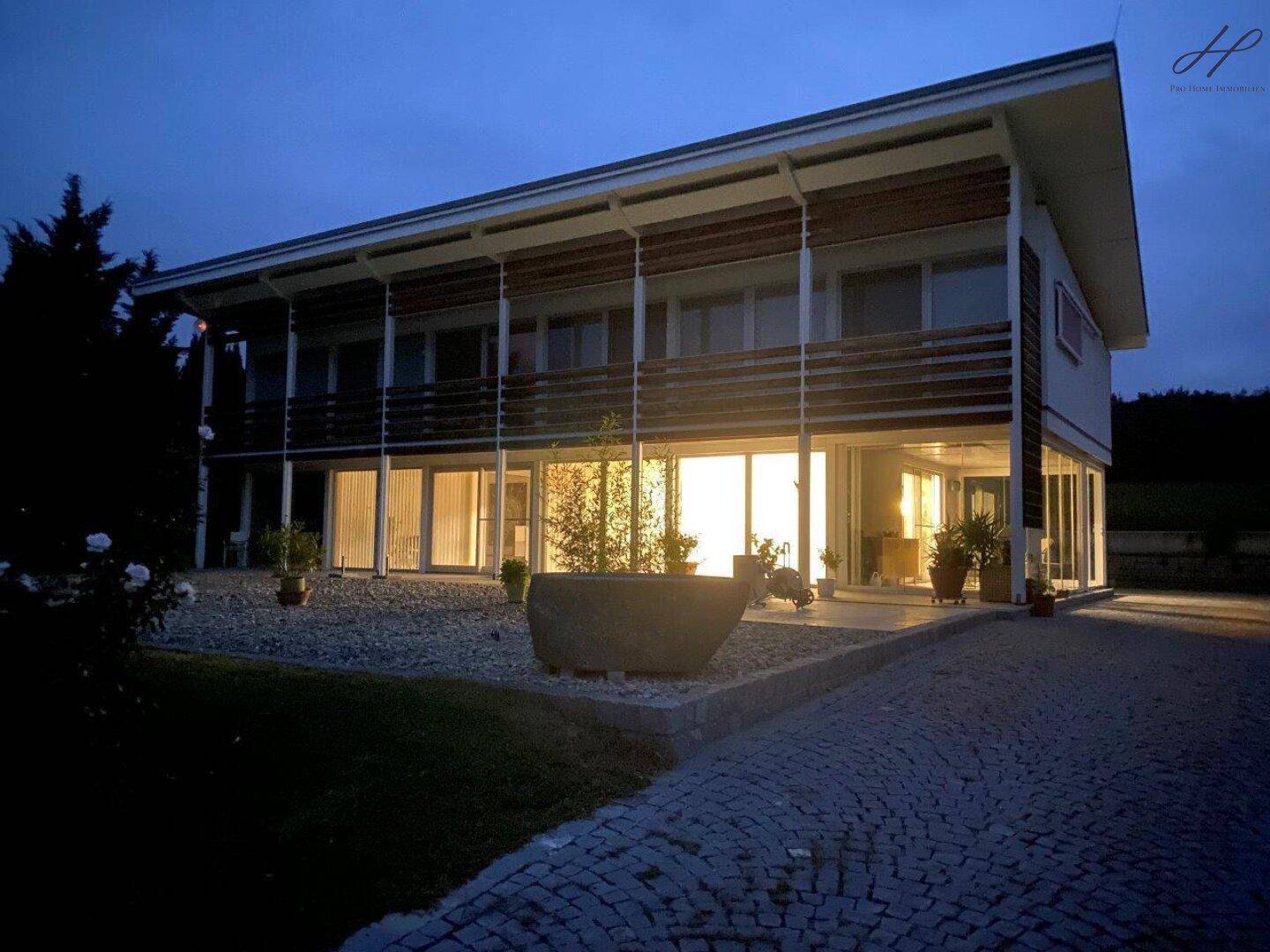 Modernes Haus bei Dämmerung mit beleuchteten Innenräumen und Außenbereich.