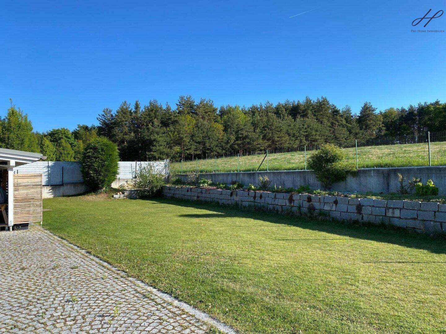 Großer Rasenbereich im Garten mit angrenzendem Wald und Steinmauer.