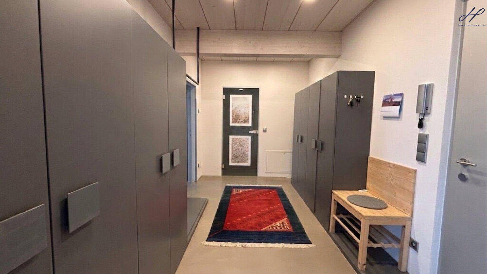Moderner Eingangsbereich mit Einbauschränken, Holzbalkendecke und einem bunten Teppich.