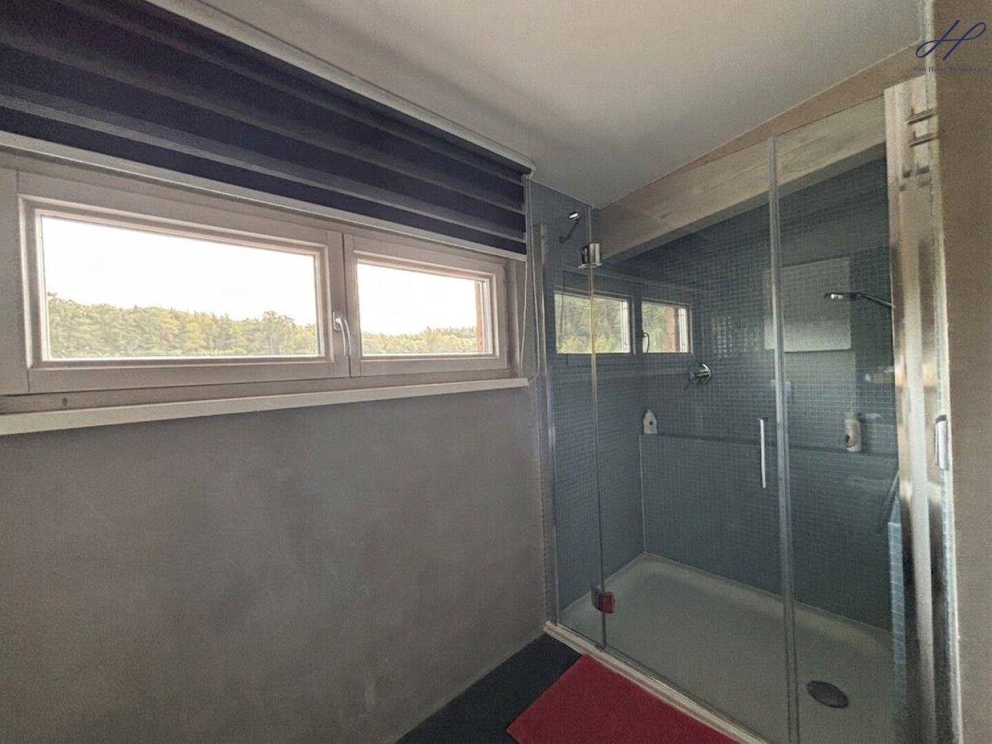 Modernes Badezimmer mit großer Duschkabine, Fliesen und Fenster mit Ausblick.