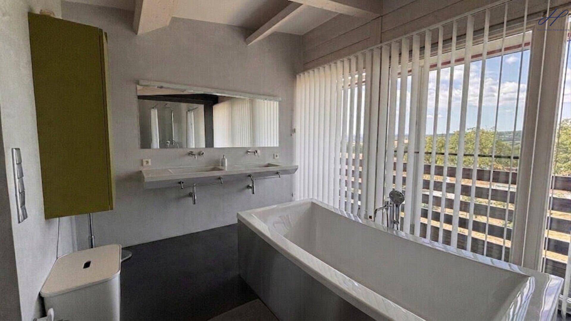 Helles Badezimmer mit Doppelwaschbecken, Badewanne und großen Fenstern.