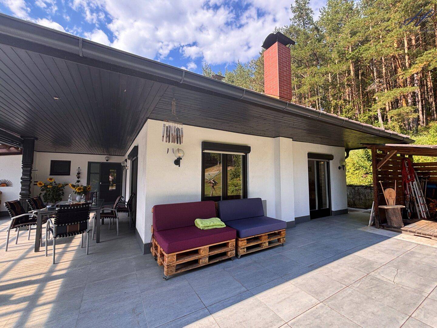 Große, sonnige Terrasse mit Palettenmöbeln und Zugang zum Haus, umgeben von Natur.