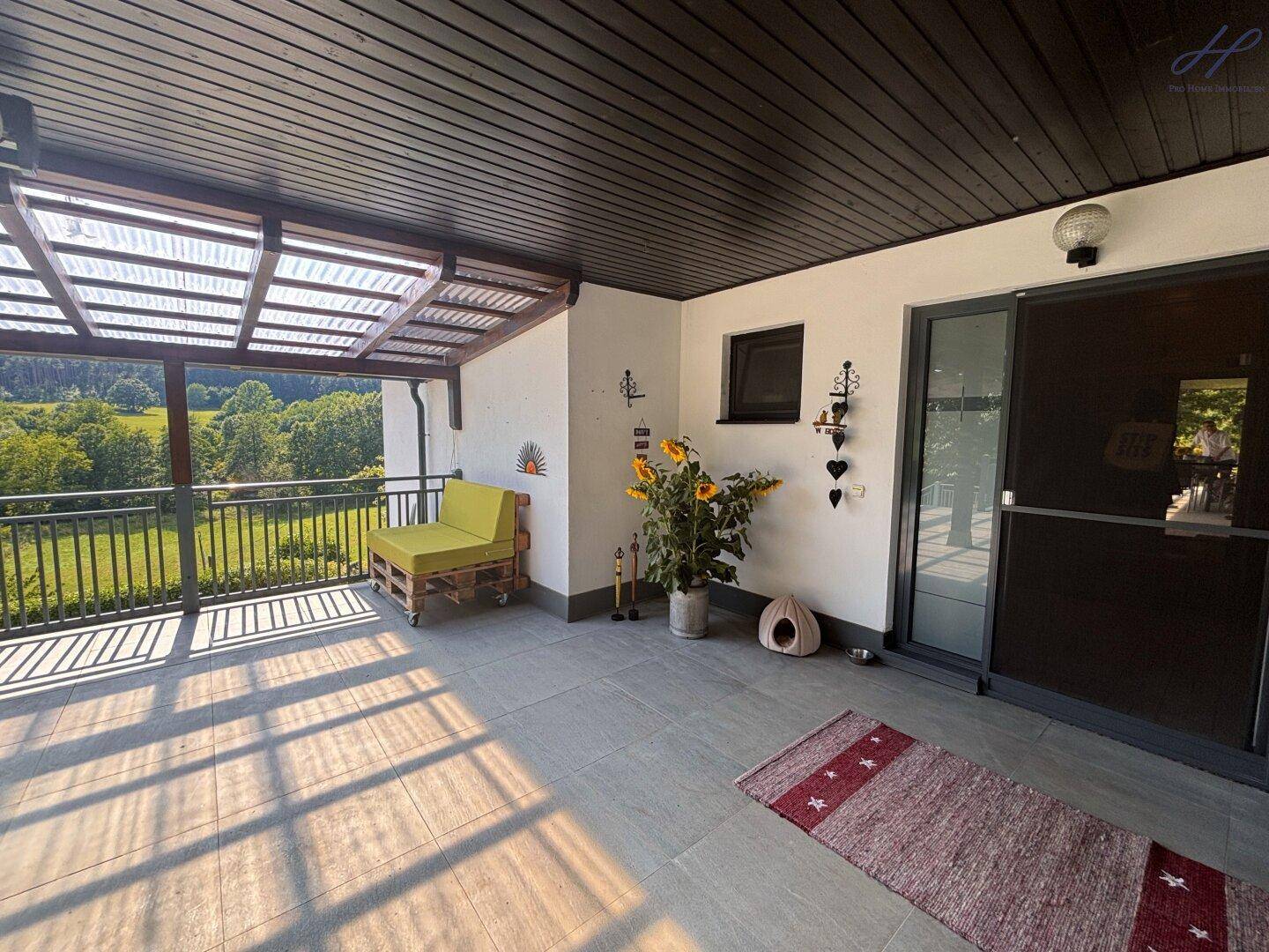 Überdachte Terrasse mit Sitzgelegenheiten und Blick auf die grüne Landschaft, direkt am Hauseingang.